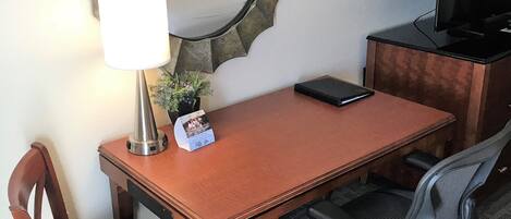 A hotel room with a wooden desk, a chair, a television, a lamp, and a mirror on the wall.