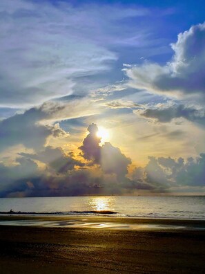 Una playa con el sol poniéndose tras las nubes, creando un efecto silueta.