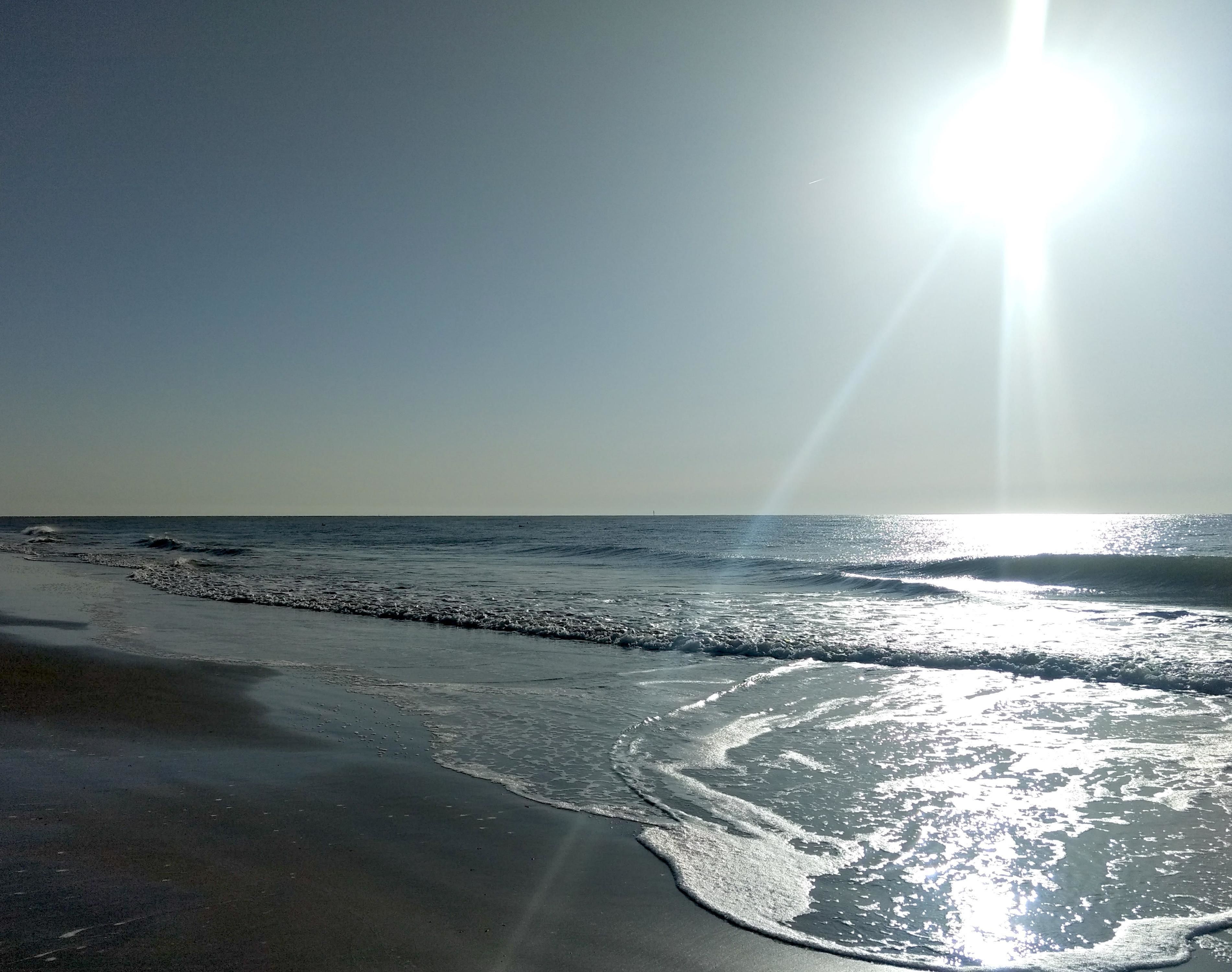 Ein Strand mit vom Wasser reflektierendem Sonnenlicht.