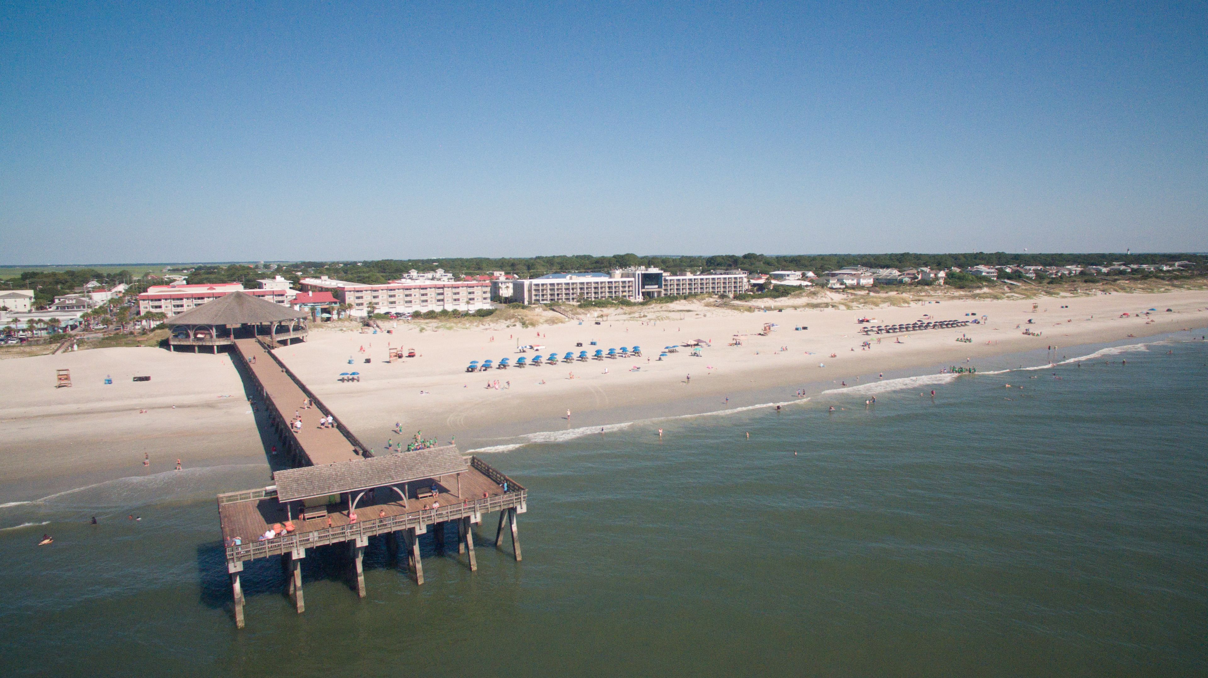 Une jetée qui s’avance dans l’eau, avec une plage et des bâtiments en arrière-plan.