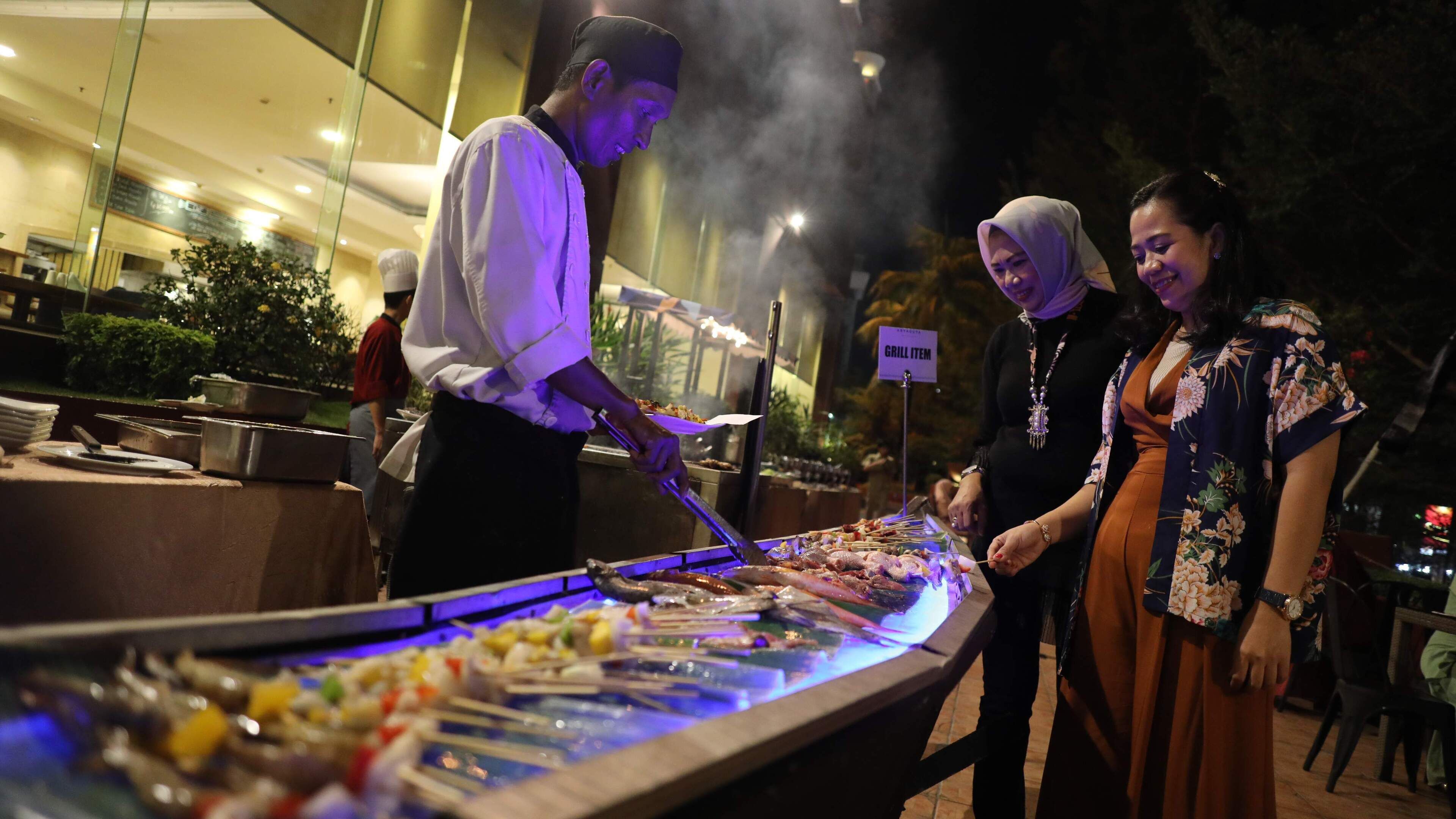 Un buffet proposant divers plats, un coin barbecue et un panneau indiquant « NOURRITURE À GRILLER ».