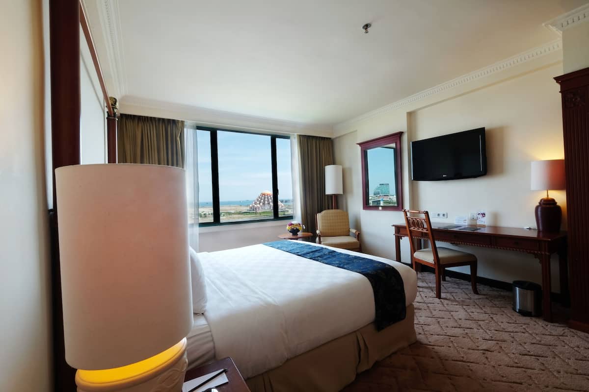 Habitación de hotel con una cama grande, un escritorio, una silla, un televisor y vistas a la ciudad.