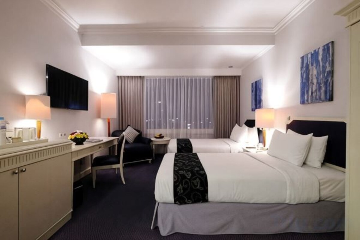 A hotel room with a bed, a desk, a chair, a television, and a window with curtains.