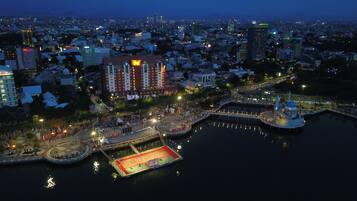 A waterfront area with a large open space, possibly for events, surrounded by buildings including a hotel with a red and white facade.