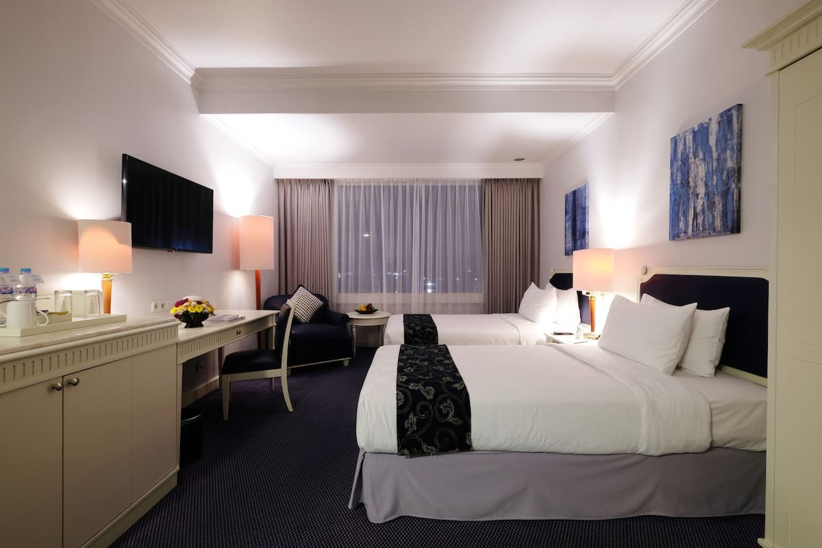 Habitación de hotel con dos camas, un escritorio, una silla, un televisor y una ventana con cortinas.