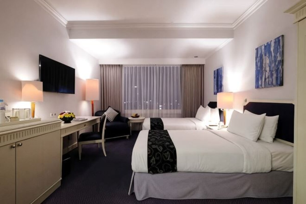 Una habitación de hotel con cama, escritorio, silla, televisor y ventana con cortinas.
