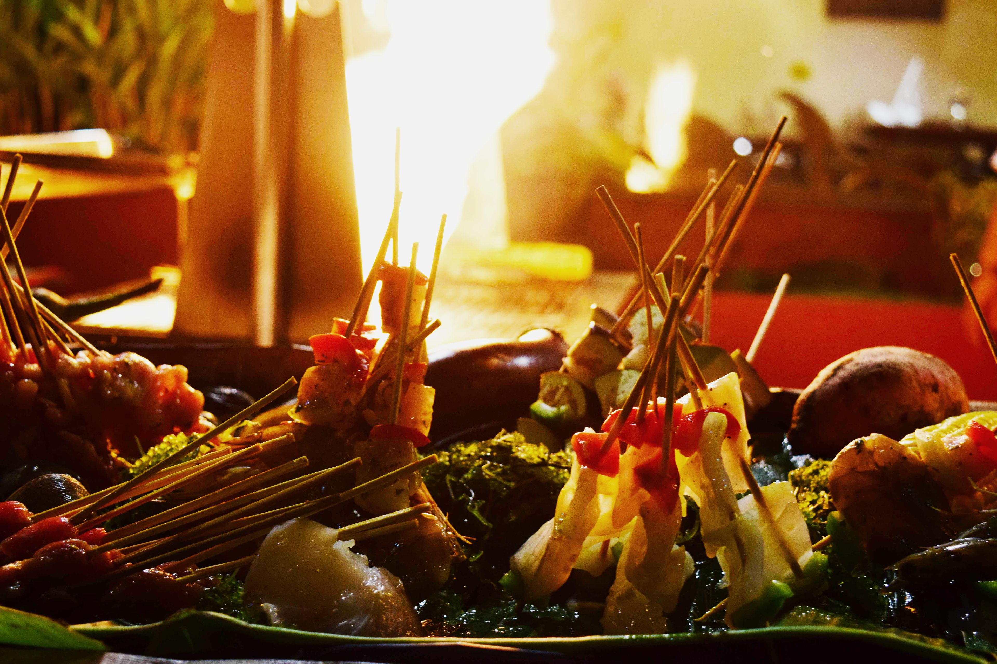 A variety of skewered foods on a platter, including vegetables and meat, in a dimly lit setting.