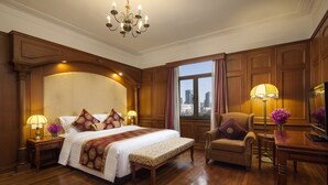 Une chambre d’hôtel avec un grand lit, un coin salon comprenant une chaise et une table, et une vue sur la ville par la fenêtre.