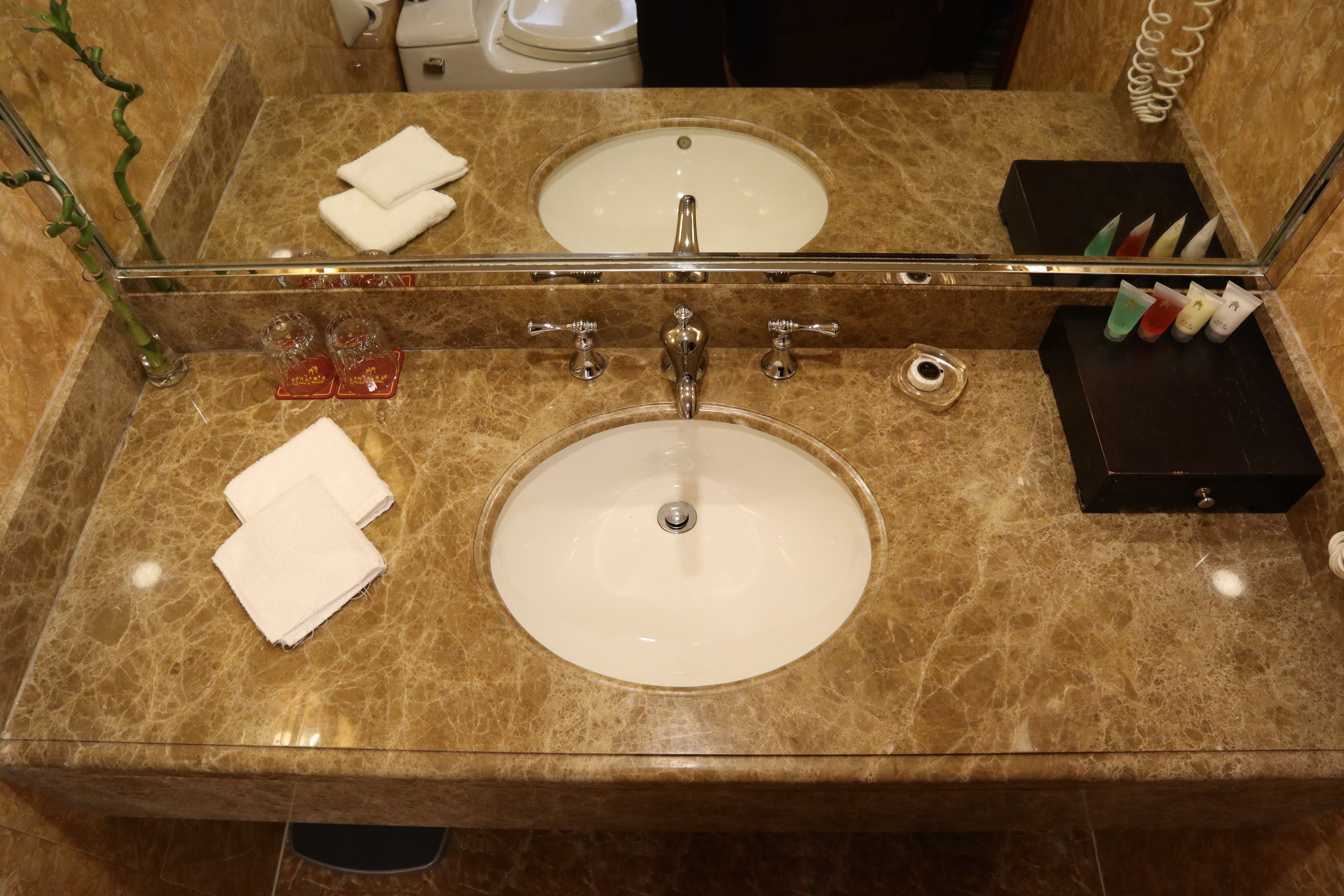 A bathroom with a marble countertop, two sinks, a glass shower enclosure, and a mirror.