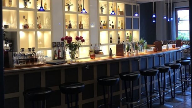 A bar area with a long counter, multiple shelves with bottles, and several stools. - Hotel ARTE Schwerin (Schwerin)