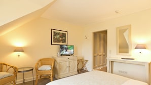 A hotel room with a bed, two wicker chairs, a small table, a TV on a cabinet, a mirror, and a fireplace. - Hotel ARTE Schwerin (Schwerin)