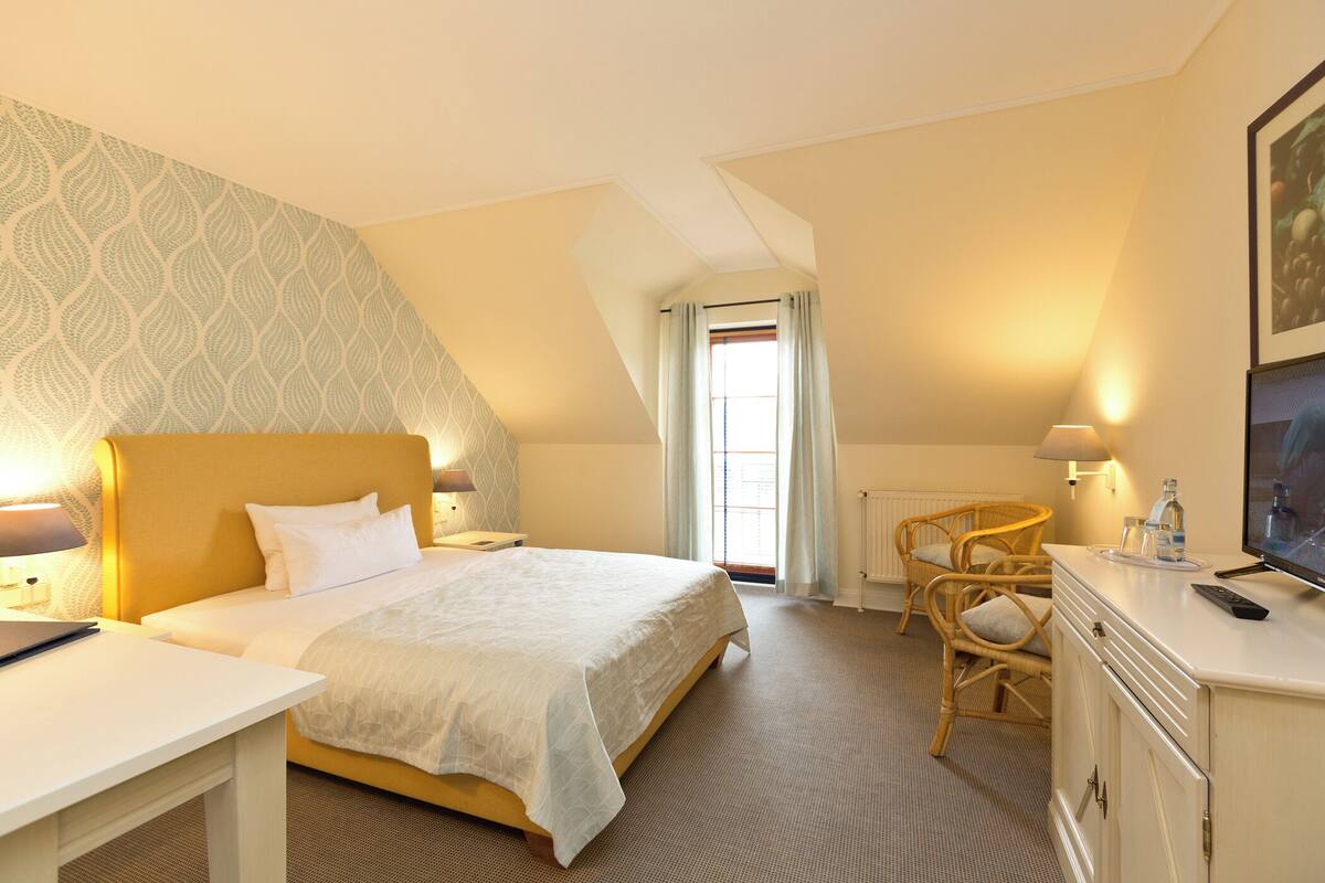 A hotel room with a bed, a desk, a chair, a TV, and a window with curtains.