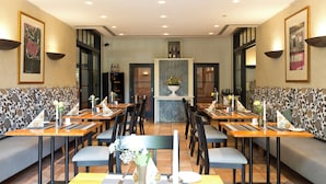 A restaurant with booths and tables, a central floral display, and wall-mounted lighting. - Hotel ARTE Schwerin (Schwerin)