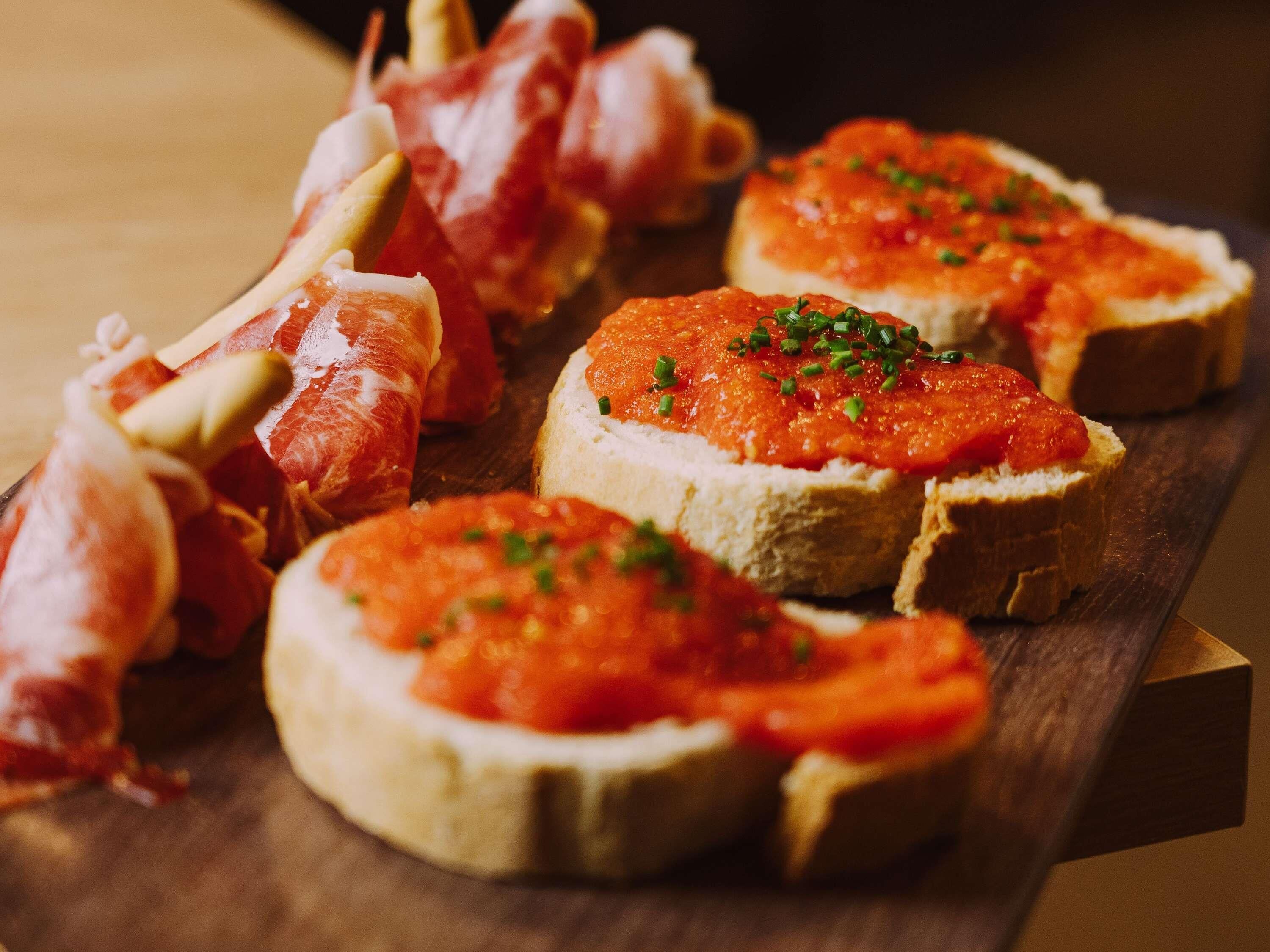 A wooden board with several pieces of bruschetta topped with tomato sauce and garnished with herbs.