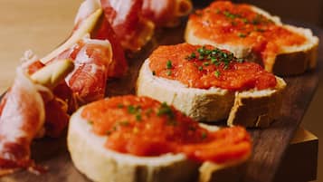 A wooden board with several pieces of bruschetta topped with tomato sauce and garnished with herbs.