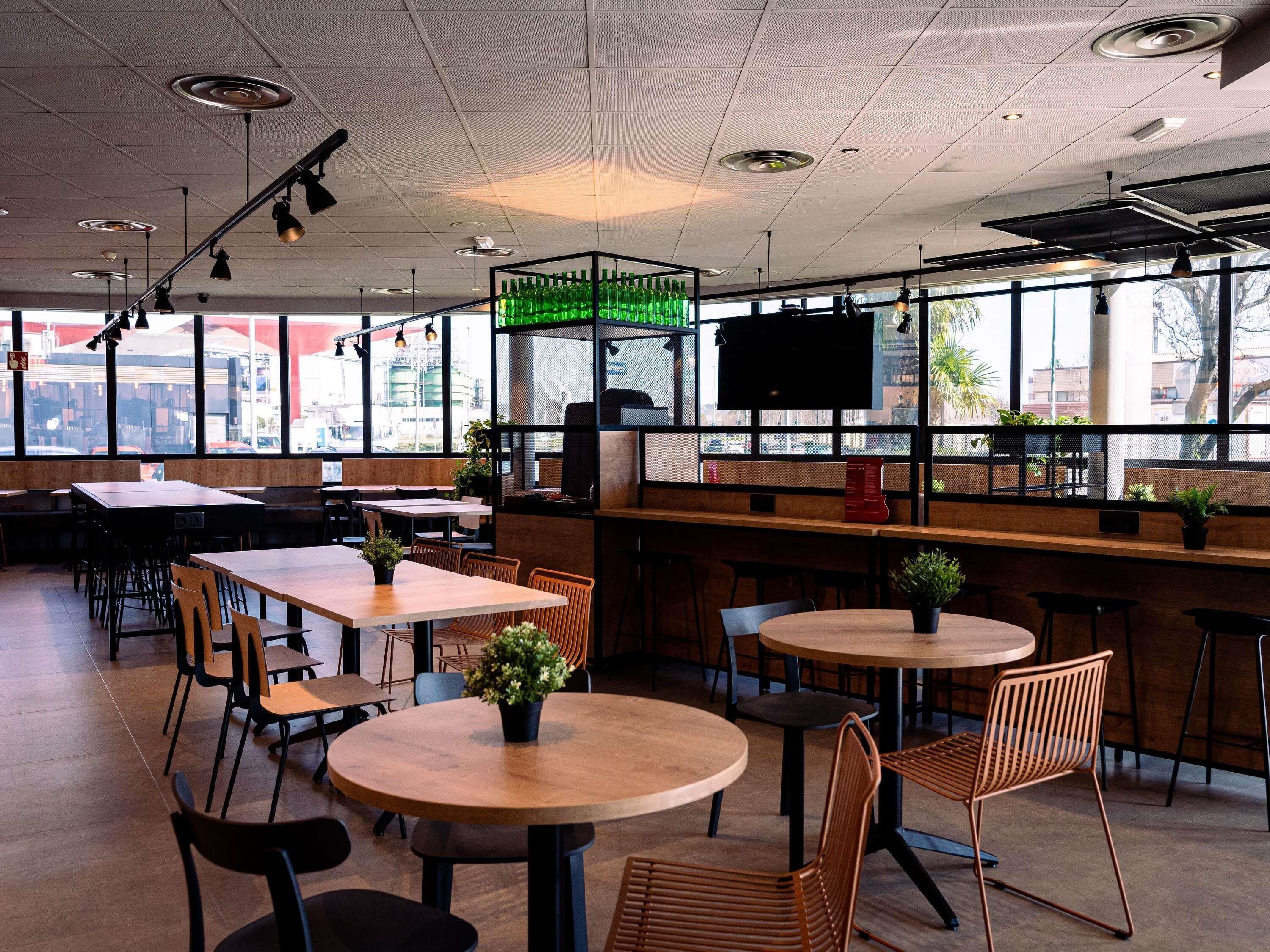 A modern restaurant interior with round tables, rectangular tables, and high ceilings with recessed lighting.