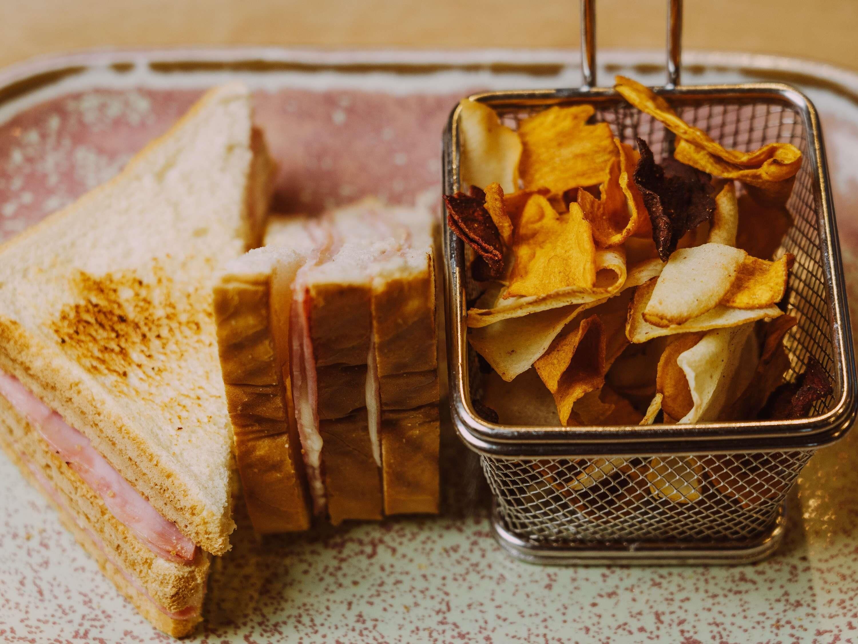 A sandwich with ham and cheese, and a basket of crispy potato chips.