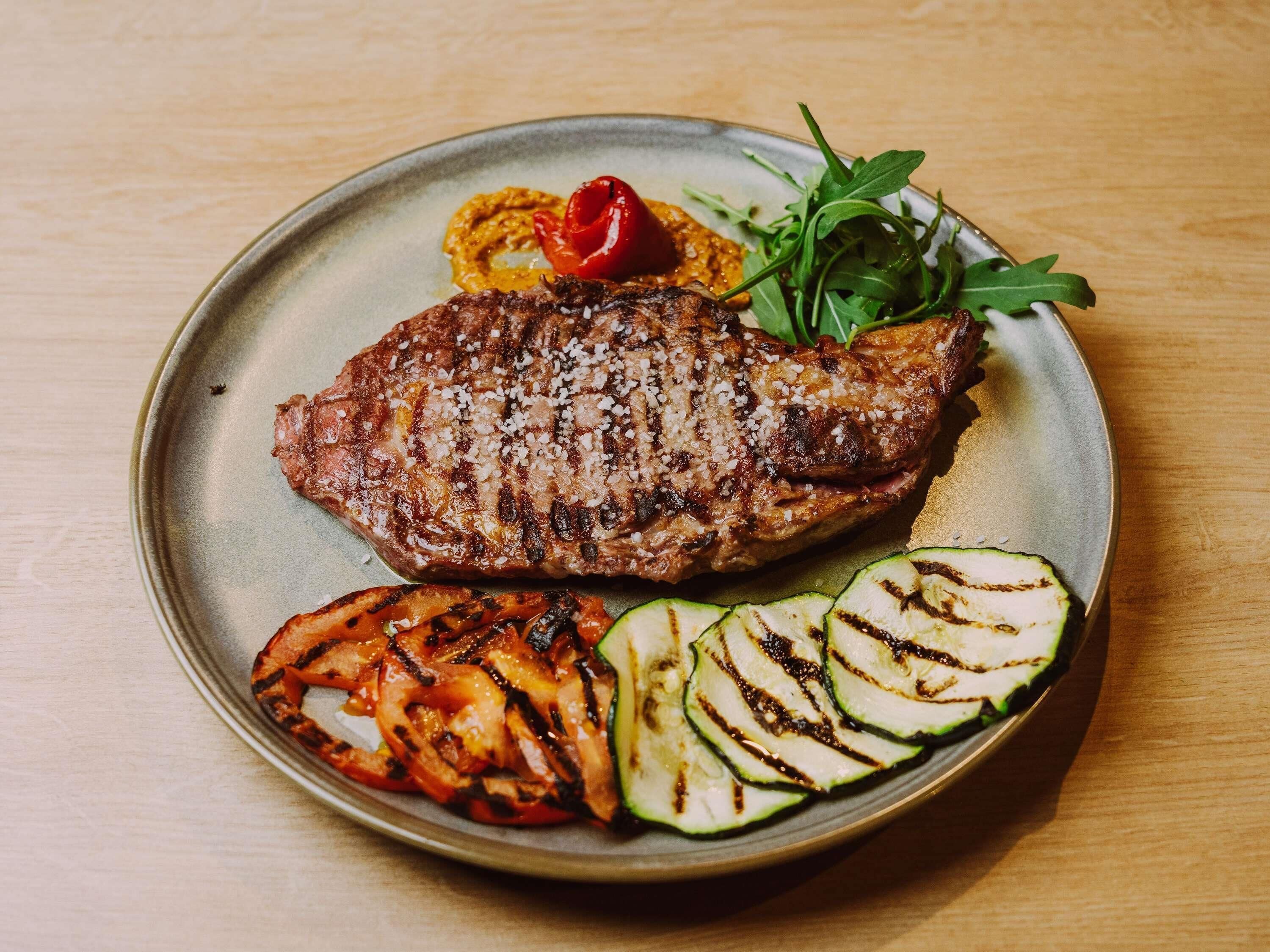 Un plato con bistec a la parrilla, verduras asadas y una salsa al lado.