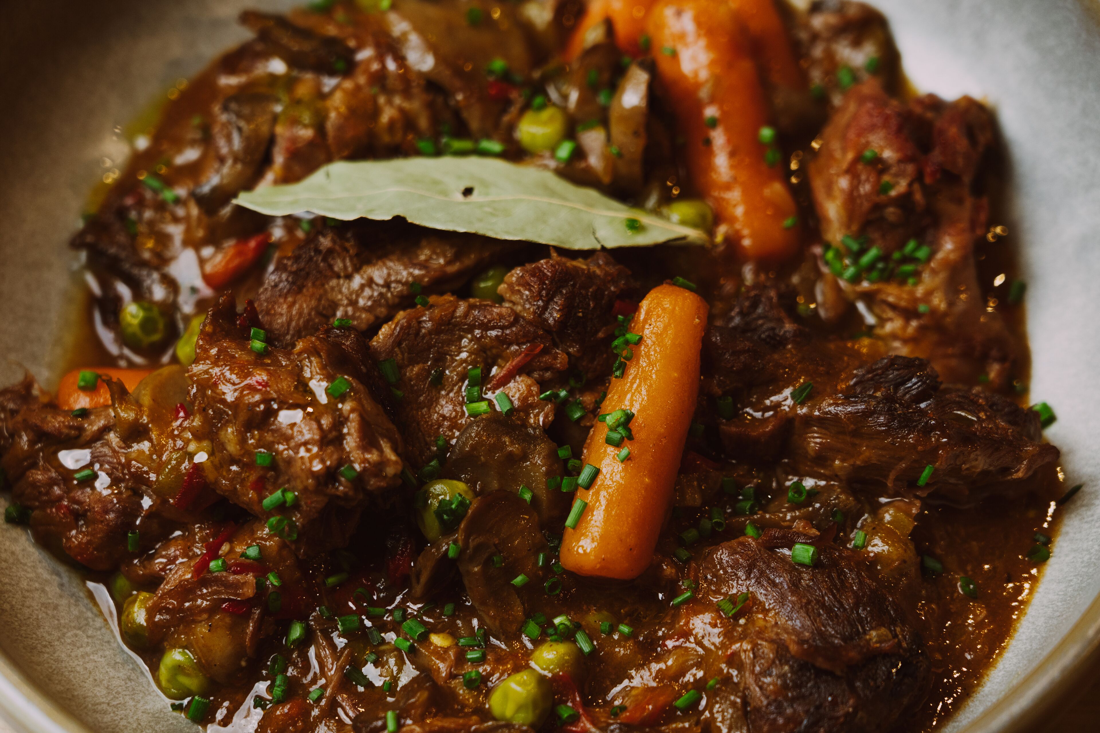 Um close-up de um ensopado de carne com cenouras e ervilhas, decorado com cebolinha picada.