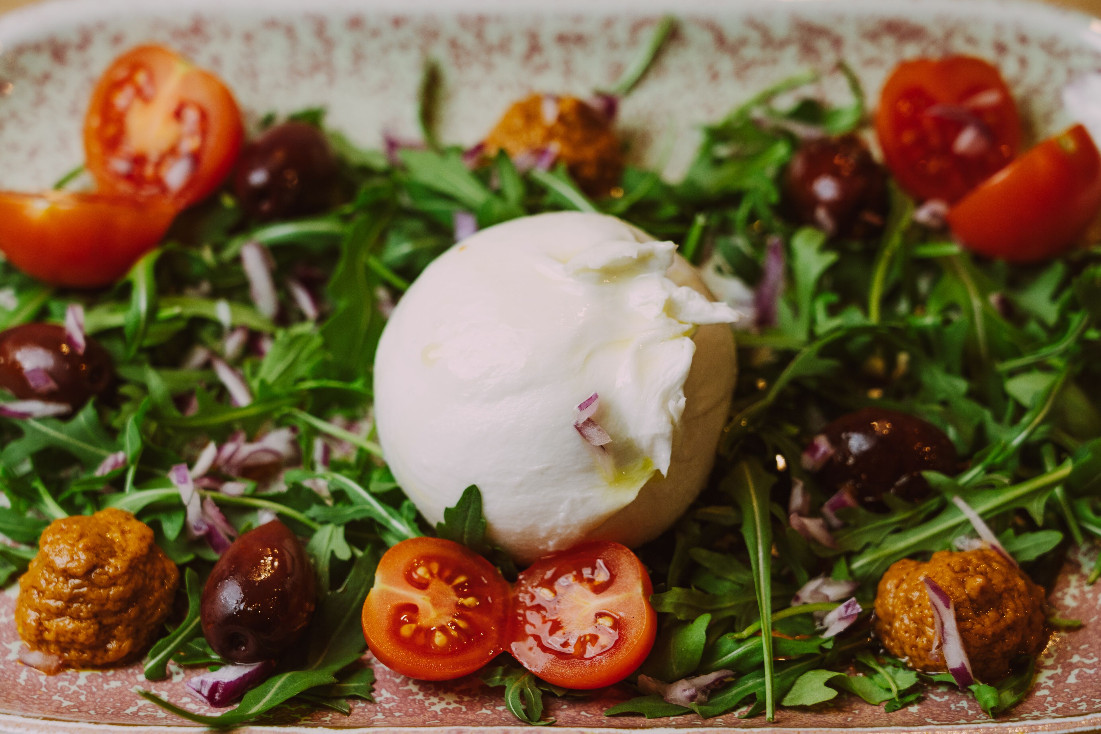 A salad with arugula, cherry tomatoes, olives, and a large mozzarella ball.