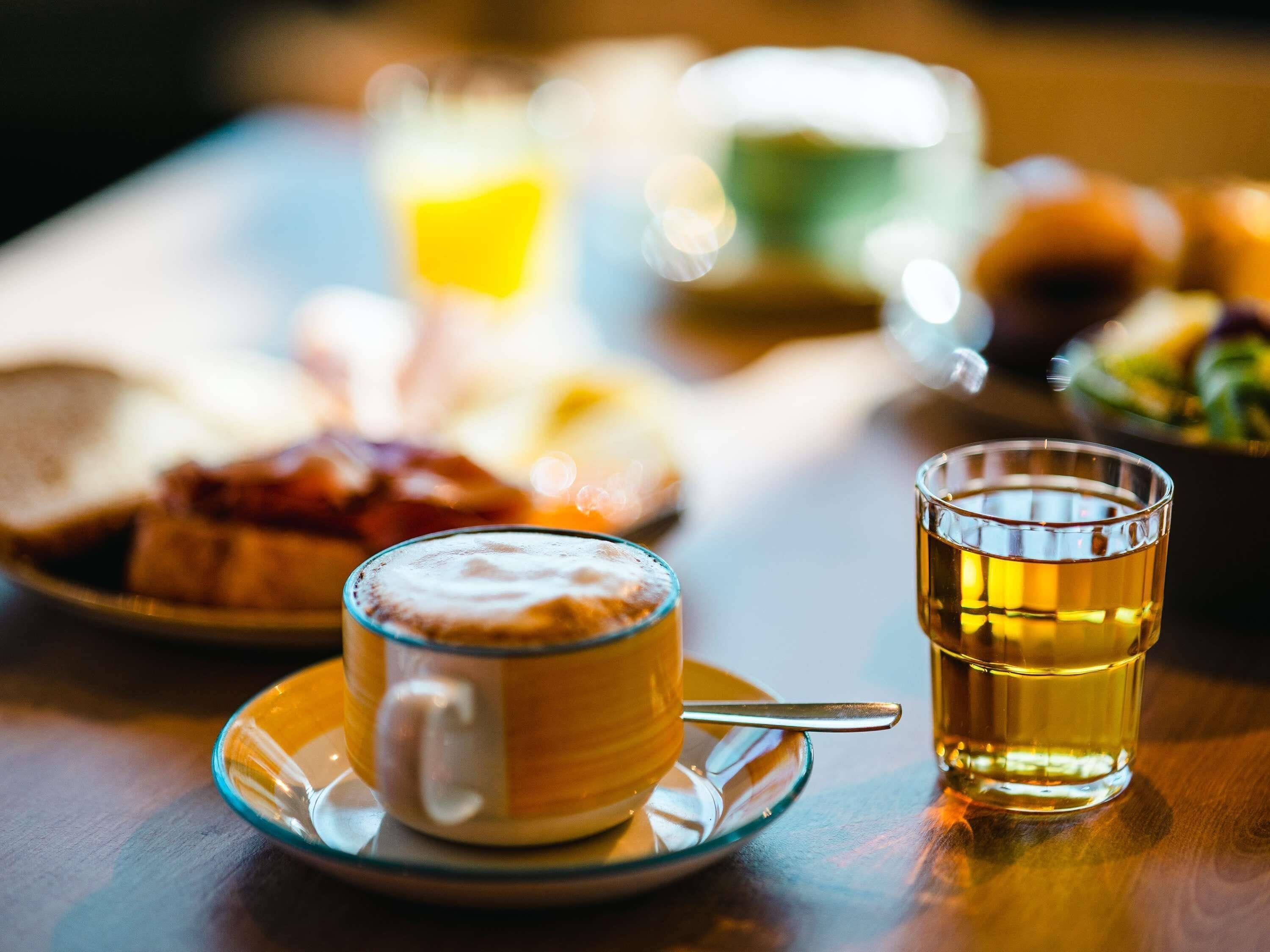 Un desayuno con una taza de café, un vaso de té y un plato de comida.