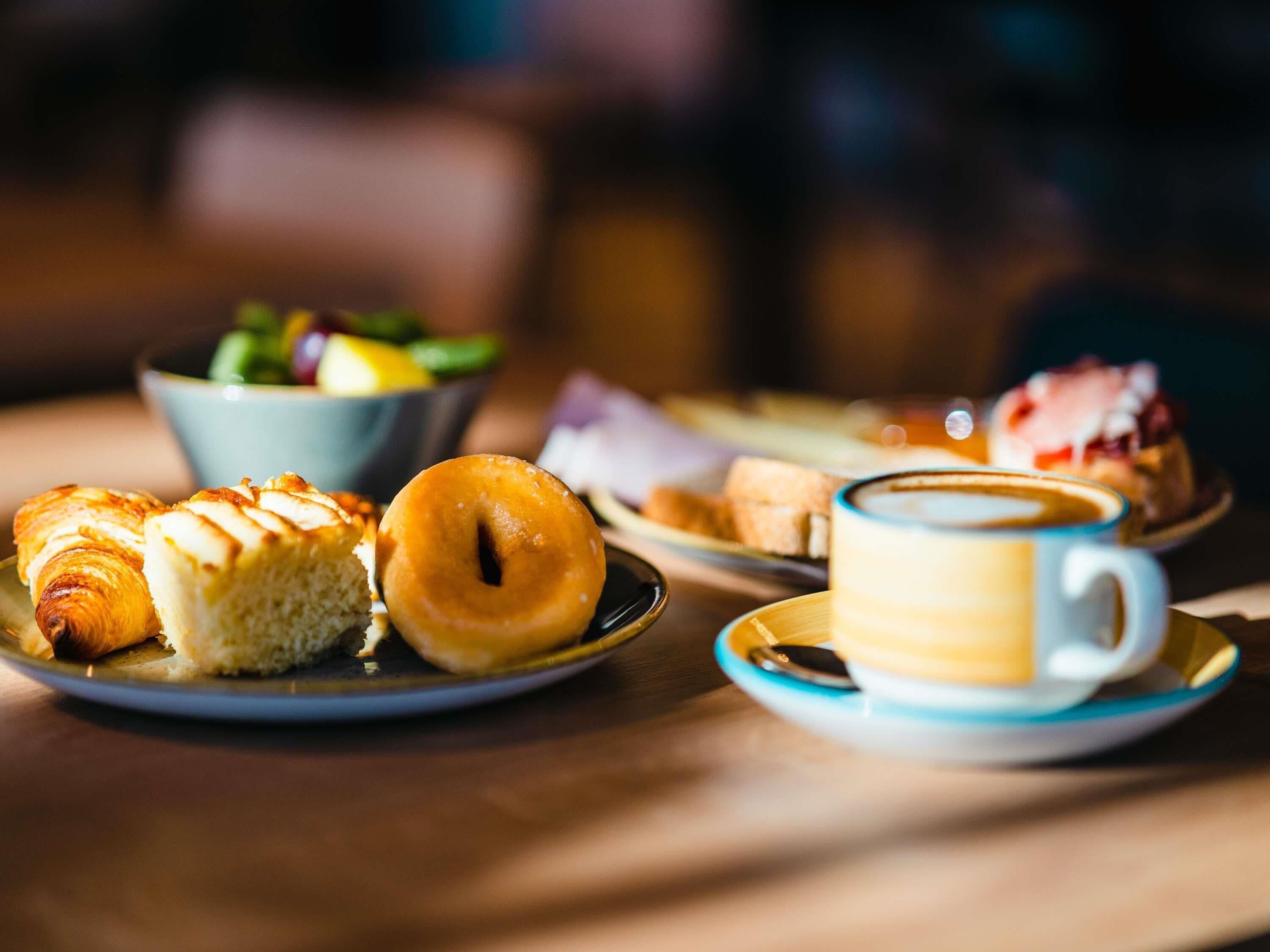 A table with pastries, a coffee cup, and a bowl of salad.