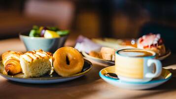A table with pastries, a coffee cup, and a bowl of salad.