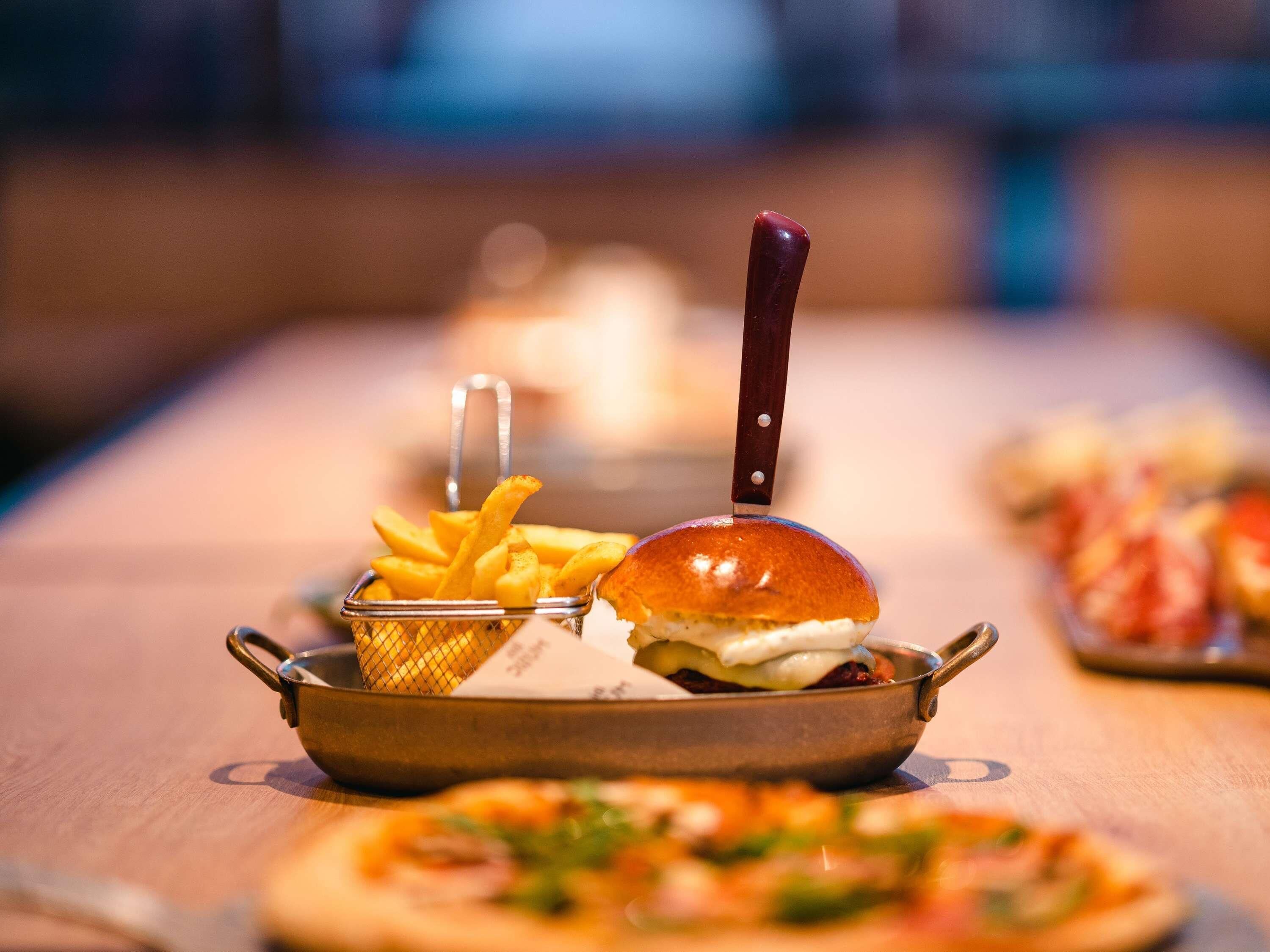 Una mesa de comedor con una comida que incluye una hamburguesa, papas fritas y una cesta pequeña de palitos de pan.