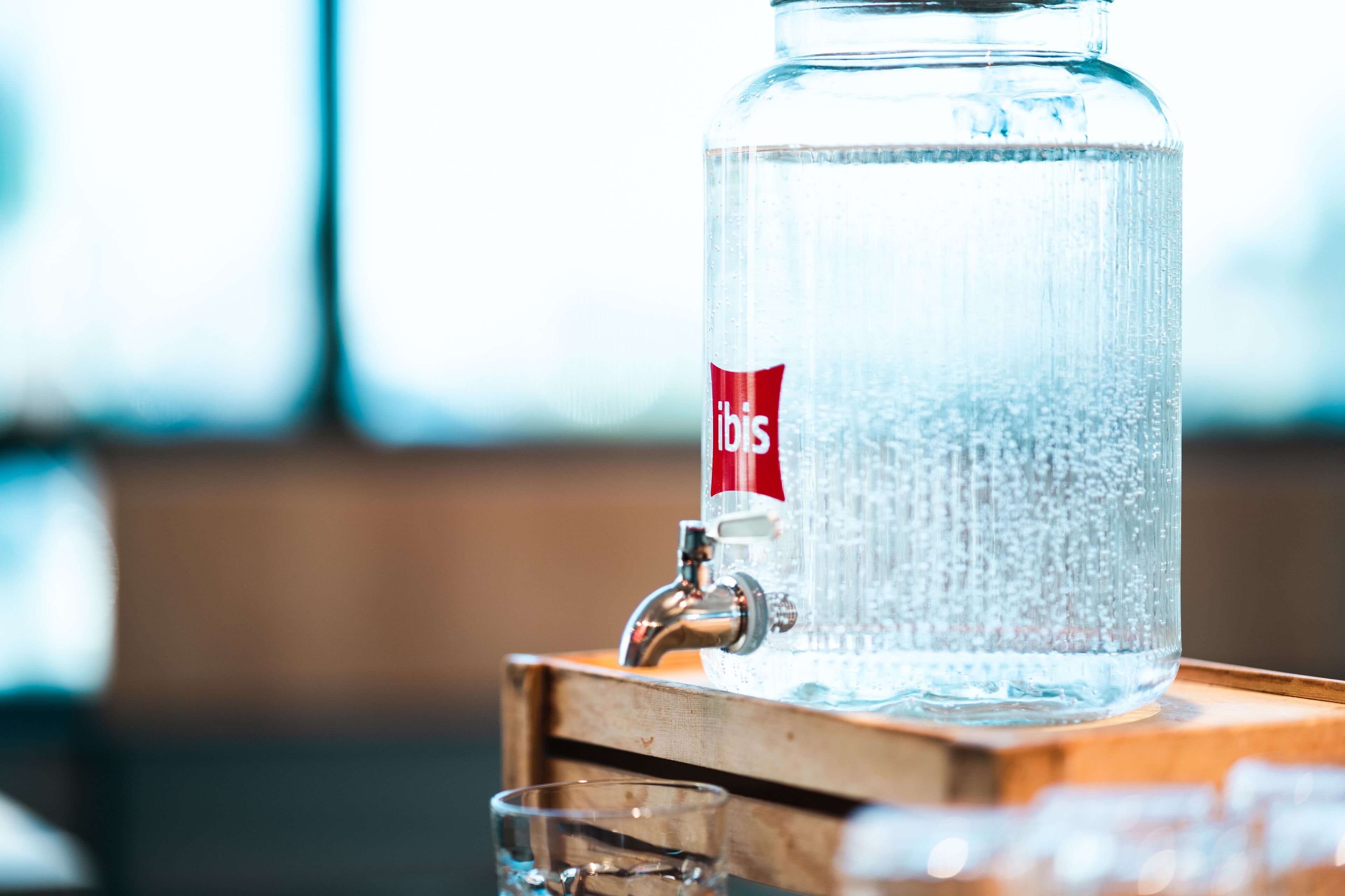 Un dispensador de agua de vidrio transparente con etiqueta roja, sobre una superficie de madera.