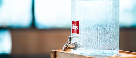 Un dispensador de agua de vidrio transparente con etiqueta roja, sobre una superficie de madera.