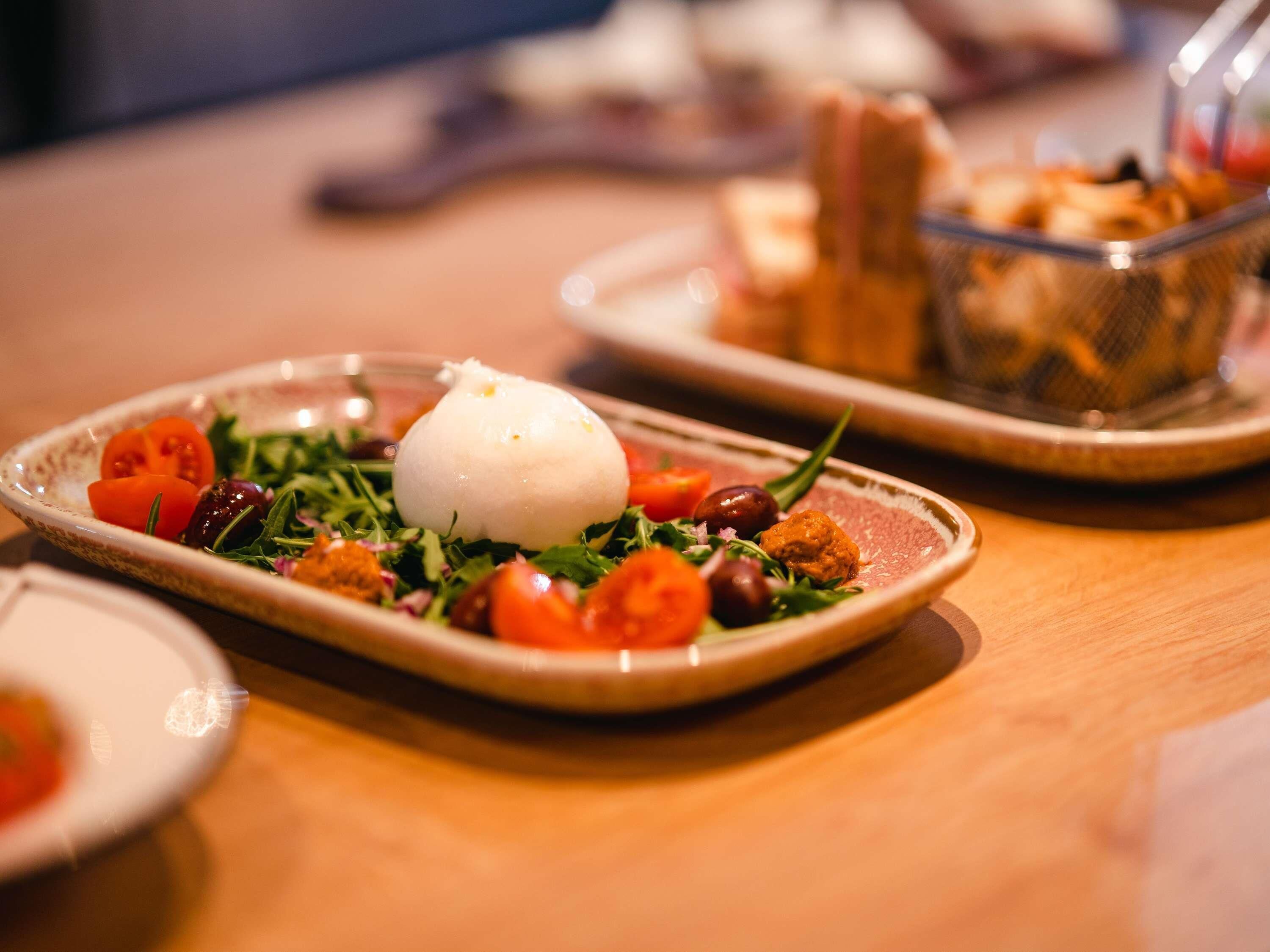A plate with a white spherical food item, cherry tomatoes, and greens on a wooden table.