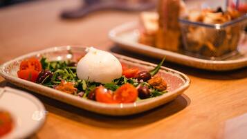 A plate with a white spherical food item, cherry tomatoes, and greens on a wooden table.