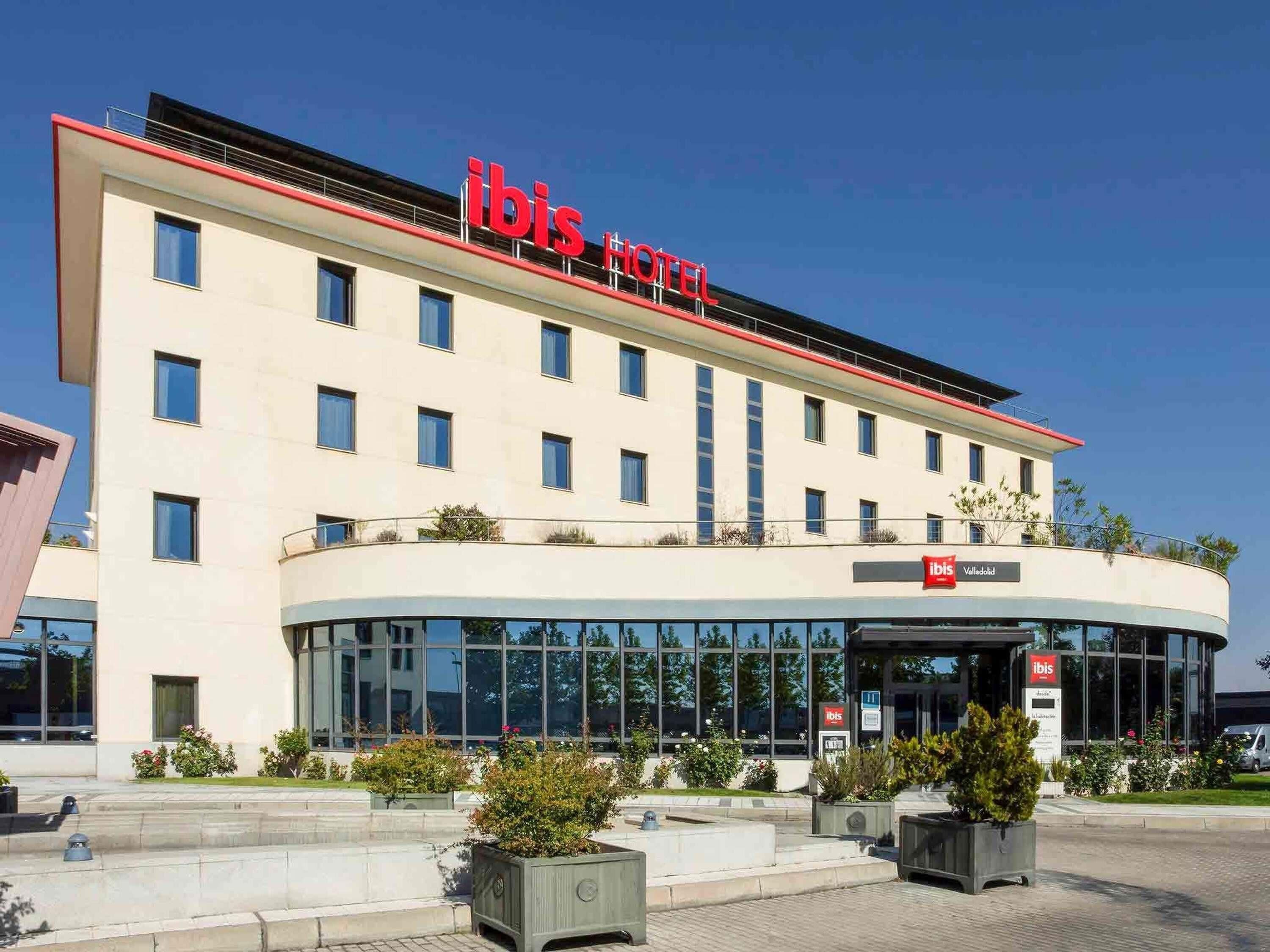 Een modern hotelgebouw met een opvallend 'ibis Hotel' bord, grote ramen en een aangelegde entree.