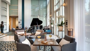 A spacious lobby with a grand piano, comfortable seating, and a large window offering a view of the outdoors.