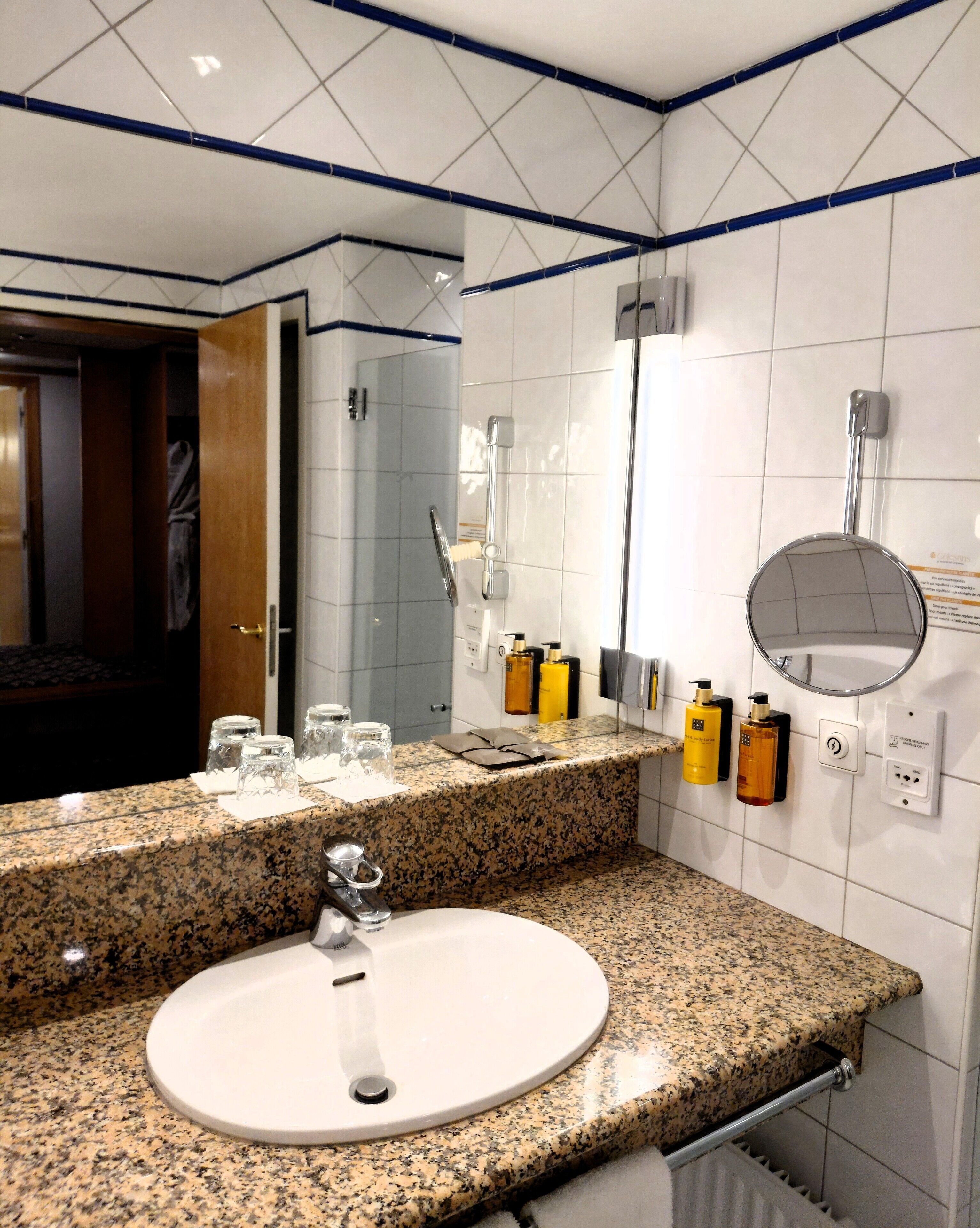 A modern bathroom with a granite countertop, a sink, a mirror, and a shower area.