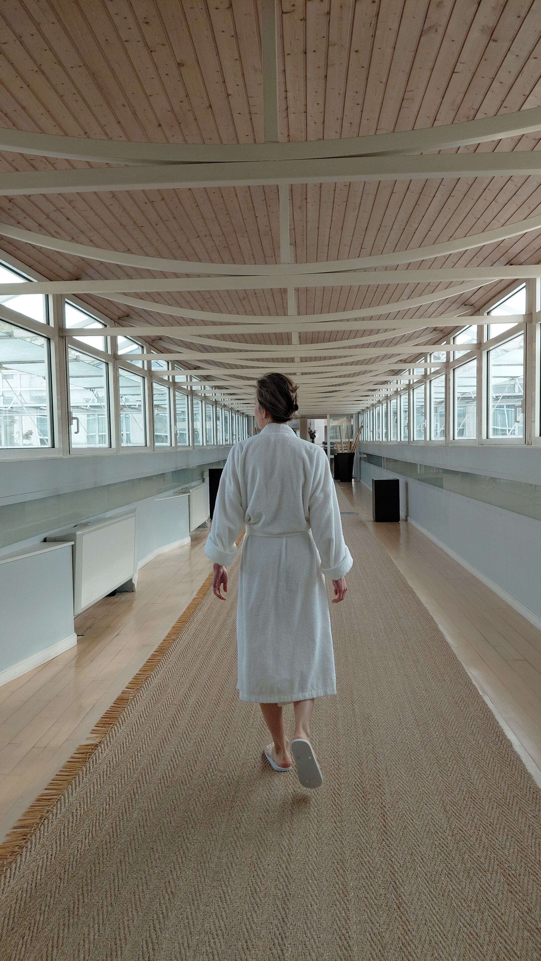 A spacious corridor with wooden ceiling beams, large windows, and a central walkway.