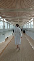A spacious corridor with wooden ceiling beams, large windows, and a central walkway.