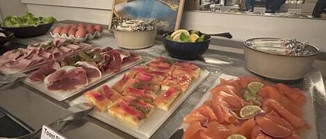 Un bufé con diferentes opciones de comida, incluyendo salmón ahumado, jamón y un plato identificado como 'Toast D'Avocat Aux Saumon Fumé'.