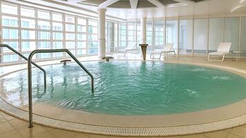 An indoor swimming pool with clear water, surrounded by a tiled floor and a high ceiling with skylights.