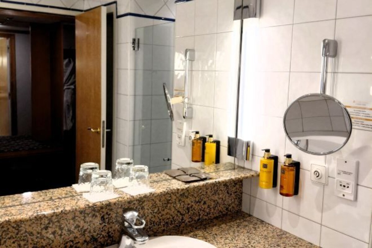 A hotel bathroom with a granite countertop, a sink, a mirror, and toiletries on the wall.