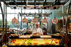 A chef preparing food in a well-lit kitchen with a variety of dishes displayed in the foreground. - Ambassador Hotel - Hsinchu (Hsinchu)