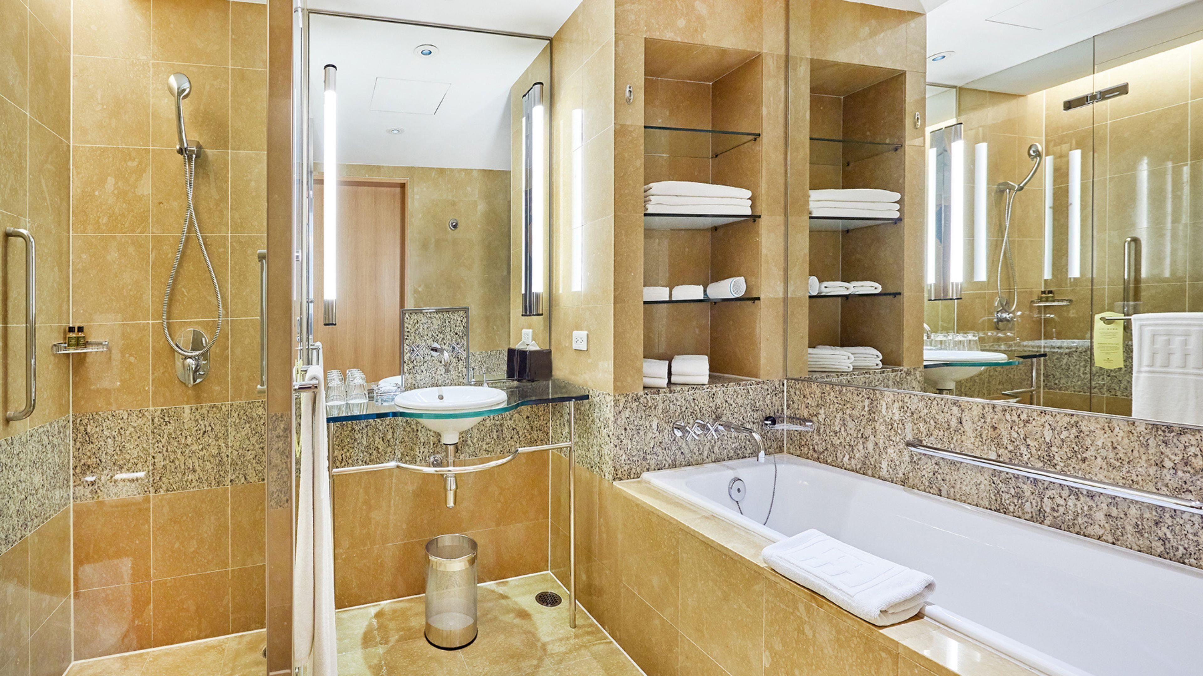 A modern bathroom with a glass shower enclosure, a freestanding bathtub, a vanity with a sink, and a glass shelf with towels.
