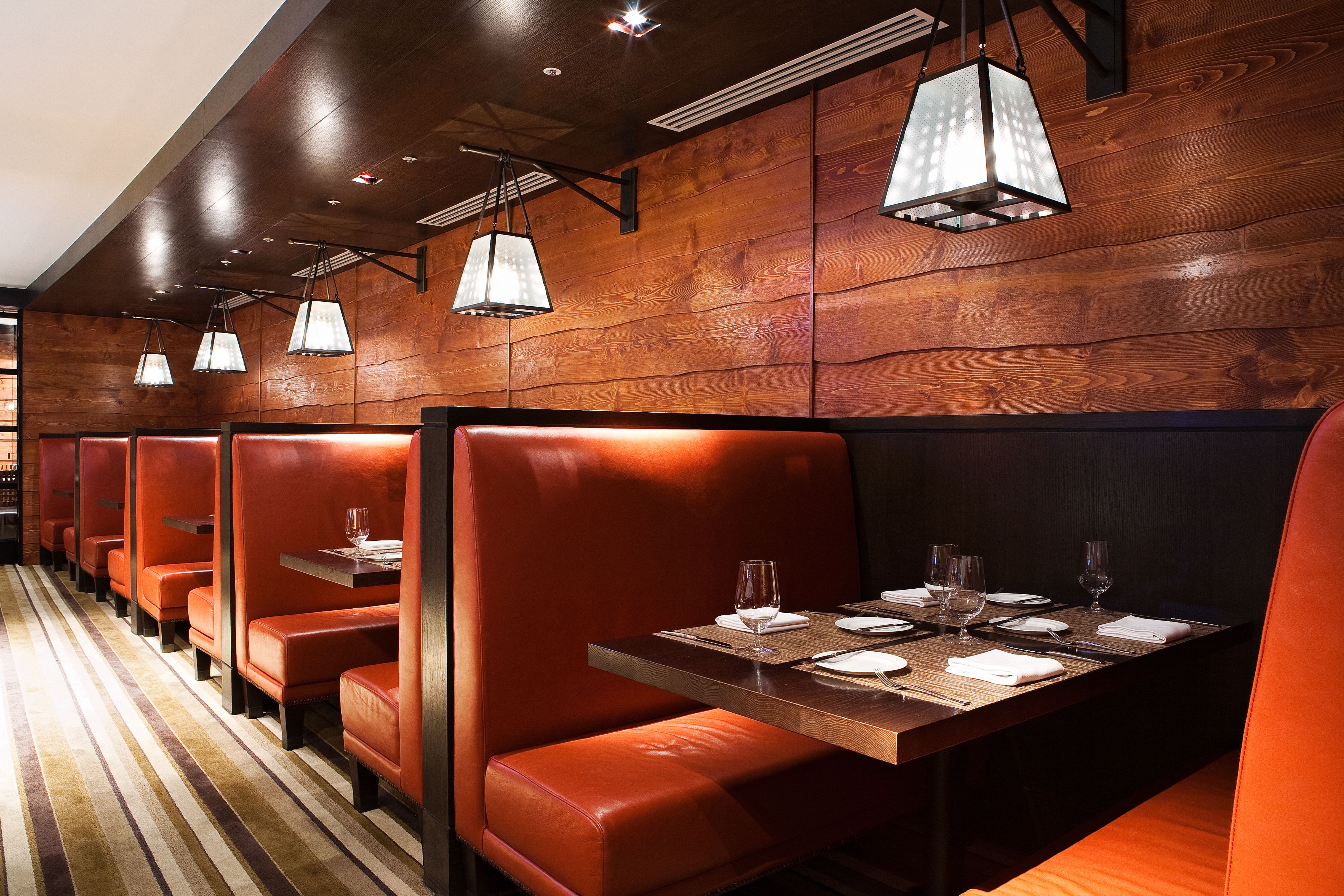 A row of booths with wooden panel walls and orange leather seating. Tables are set with white tablecloths, plates, and glasses.