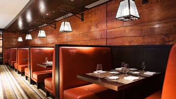 A row of booths with wooden panel walls and orange leather seating. Tables are set with white tablecloths, plates, and glasses.