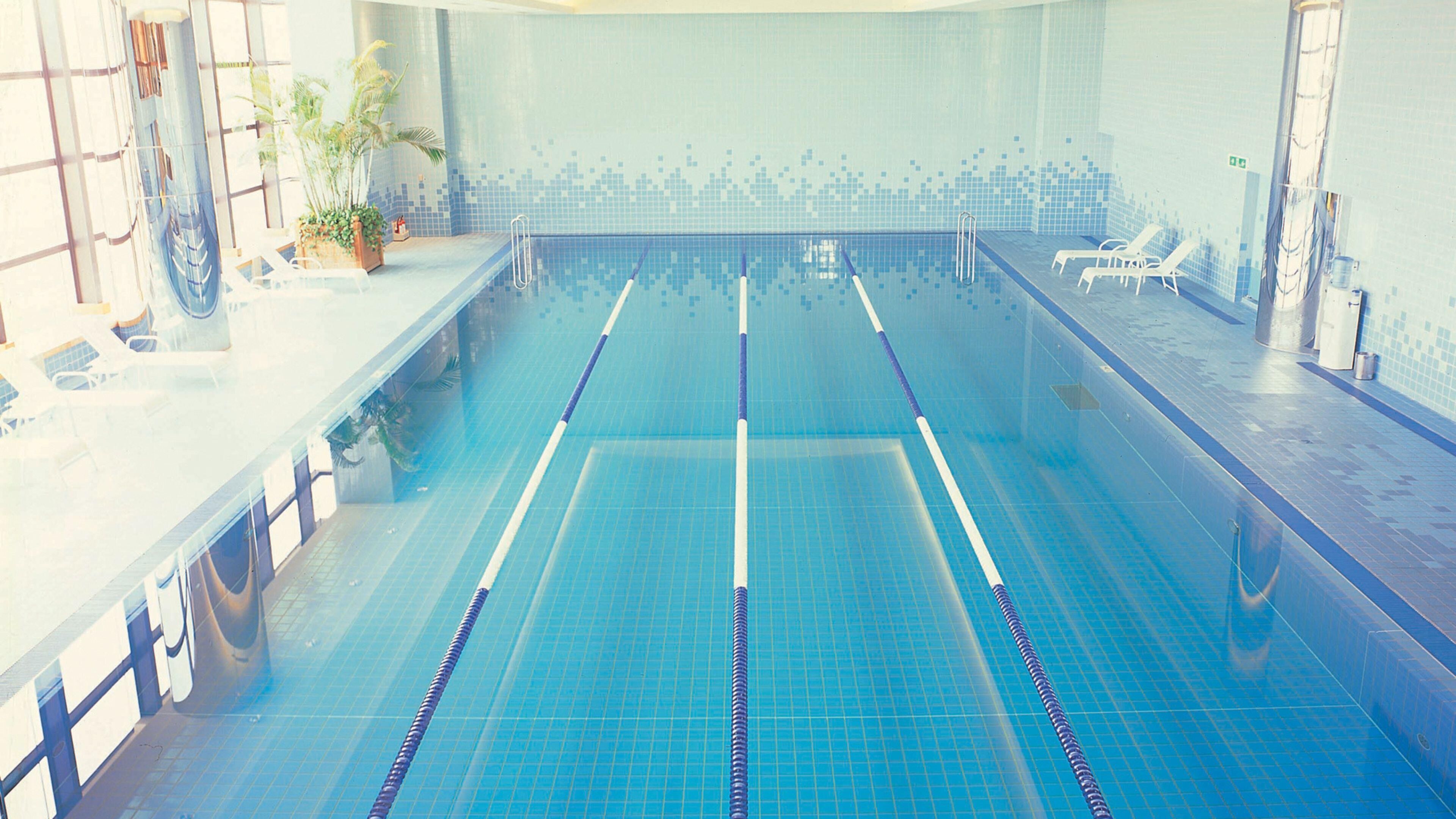 Una piscina con carriles delimitados, un muro de azulejos y sillas de descanso en un lateral.