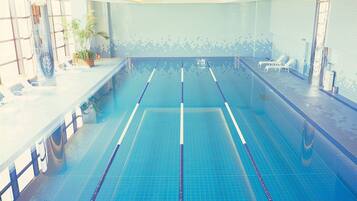 Una piscina con carriles delimitados, un muro de azulejos y sillas de descanso en un lateral.