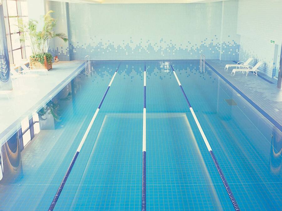 Una piscina con carriles delimitados, un muro de azulejos y sillas de descanso en un lateral.