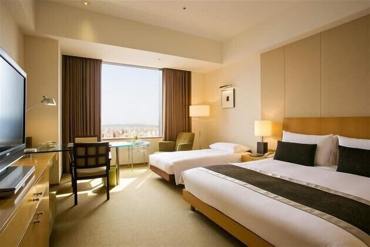 A hotel room with two beds, a desk, a chair, a TV, and a window with curtains.