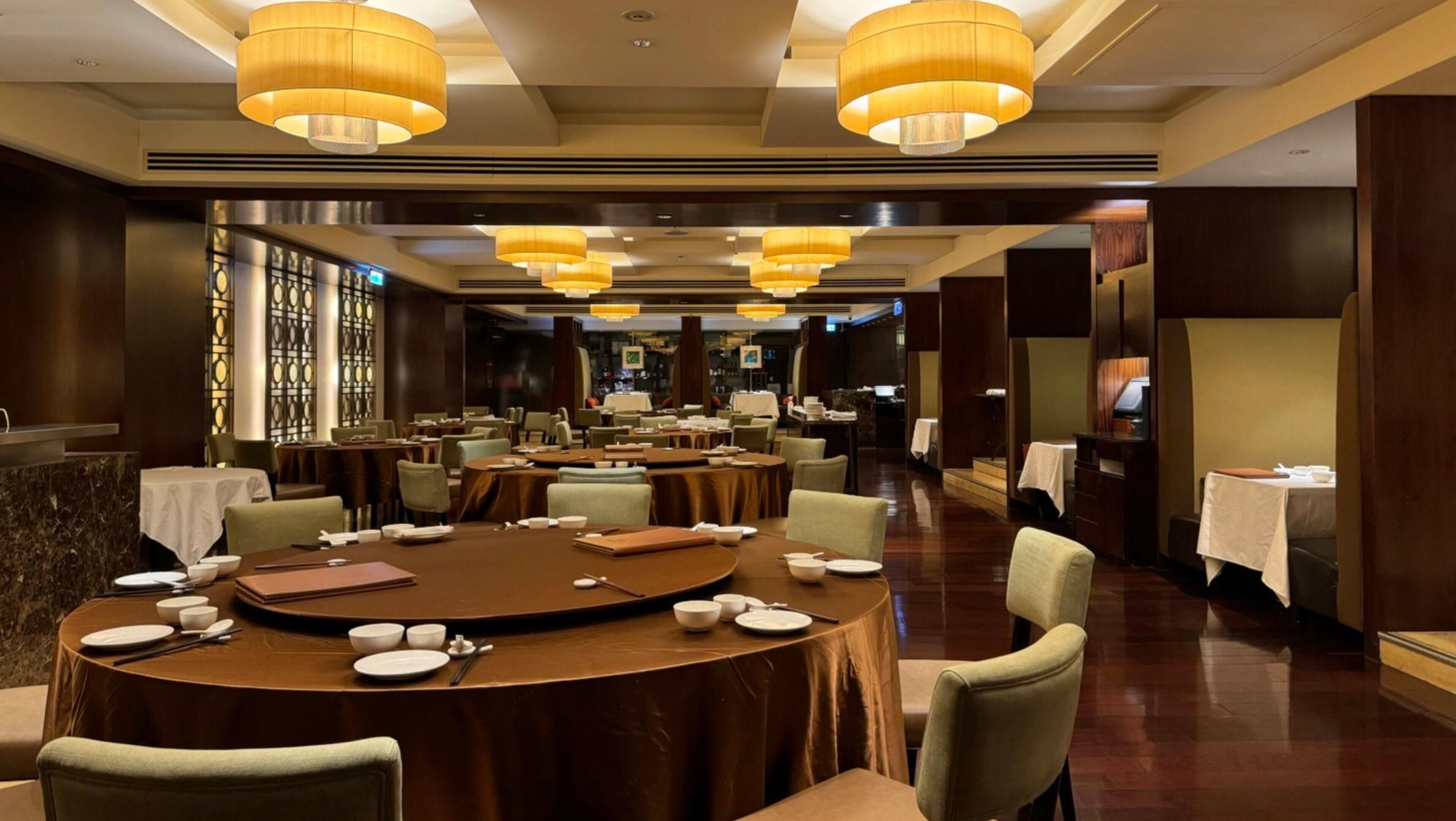 A spacious dining area with round tables, chairs, and warm lighting.