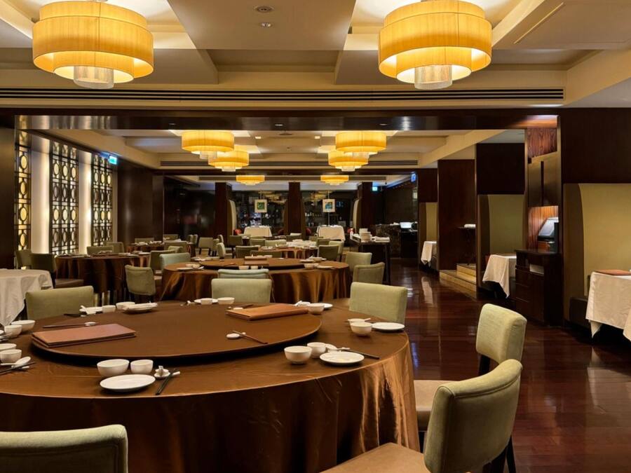 A spacious dining area with round tables, chairs, and warm lighting.